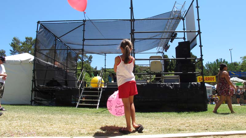 Girl with pink balloon watches from the side of the stage